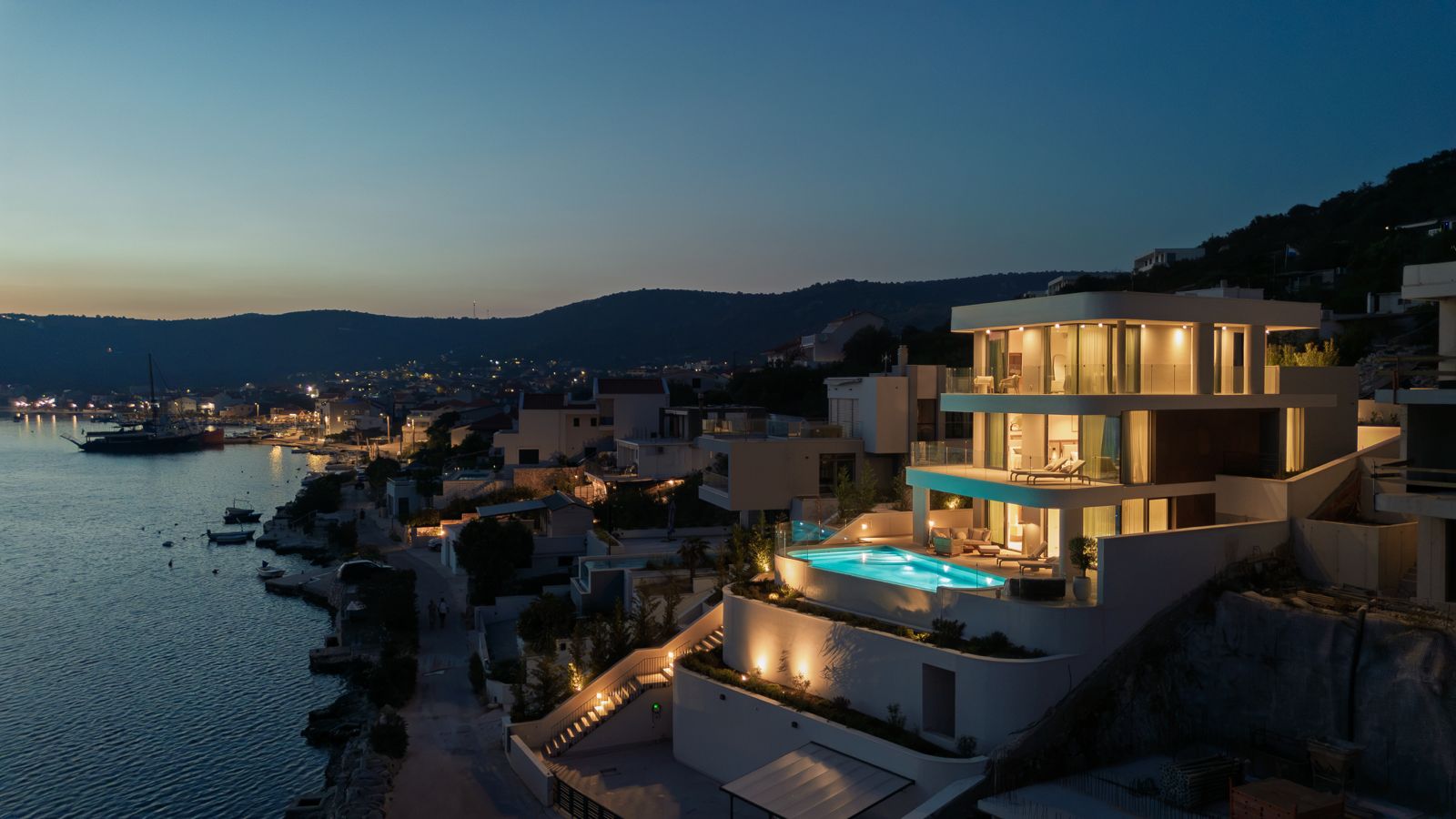 Villa Dream Aura illuminated at dusk above the waterfront, with its pool and terraces overlooking the bay